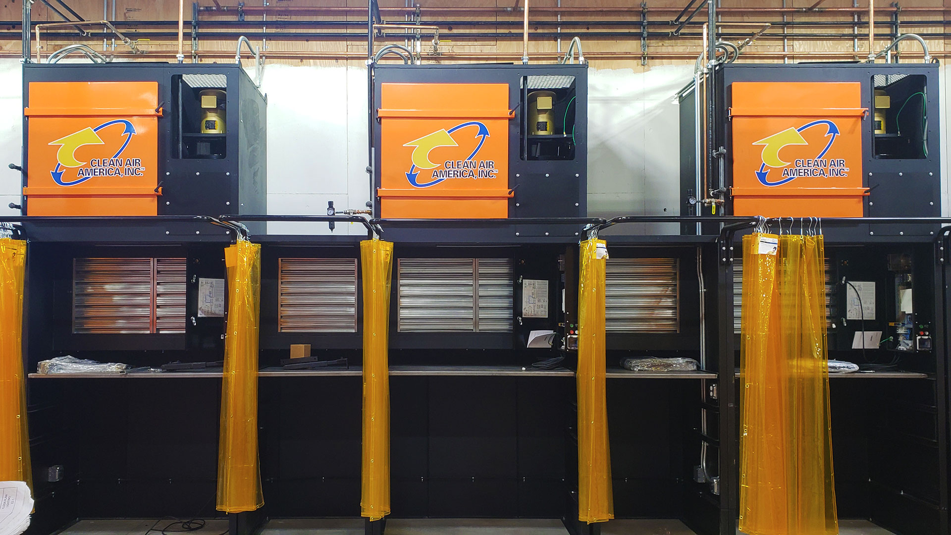 Three welding booths side-by-side with orange drapes open.