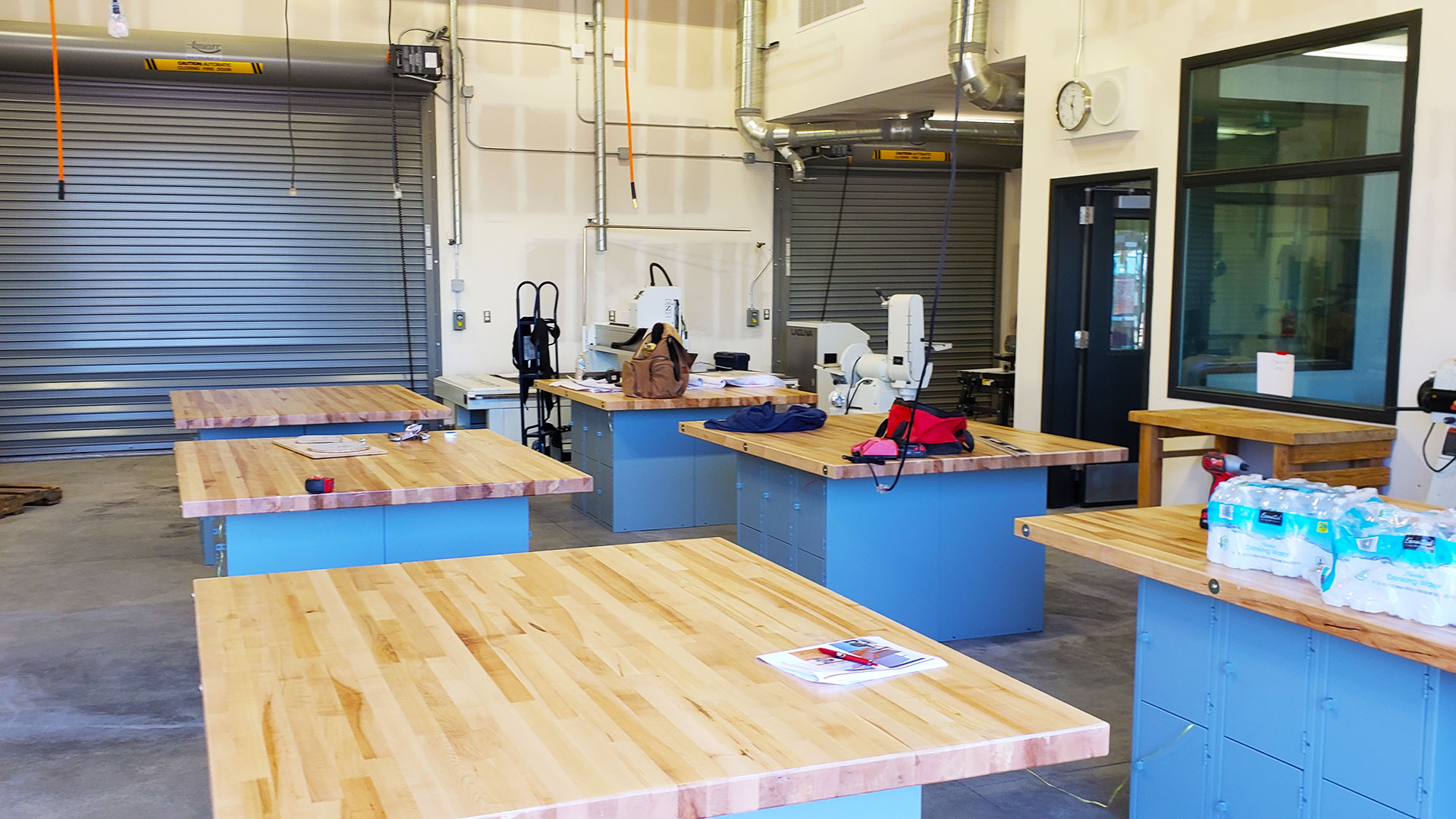 Series of 6 tables in wood shop, roll up shop doors in background.