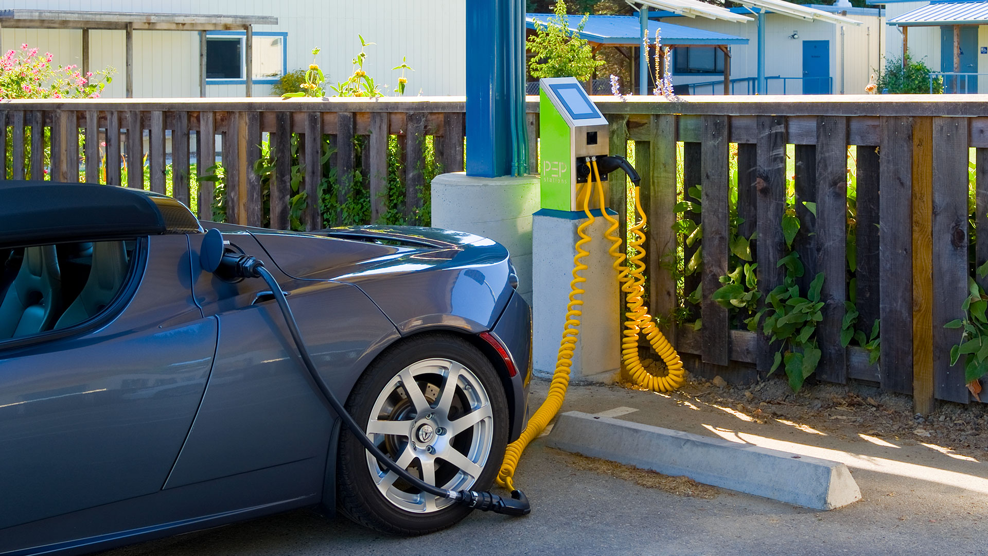 Car charging station under solar panels, with electric car parked in front using the station.