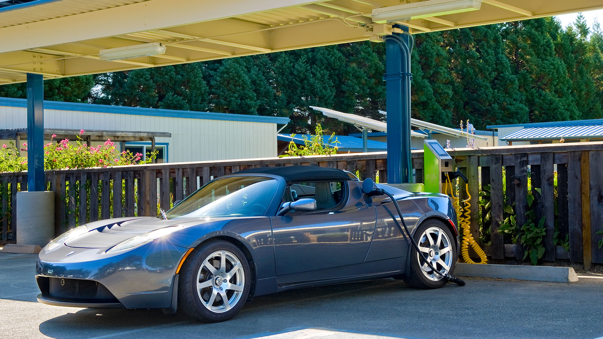 Car charging station under solar panels, with electric car parked in front using the station.