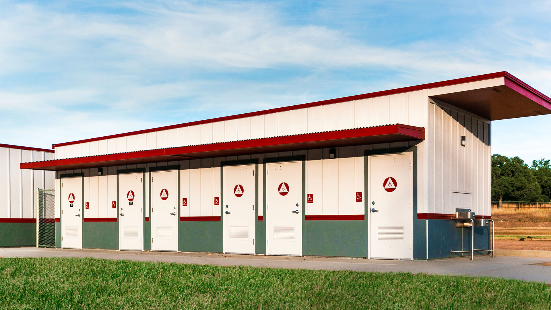 Portable restroom building with white panel walls and gray wainscot, with concrete walkway and grass.