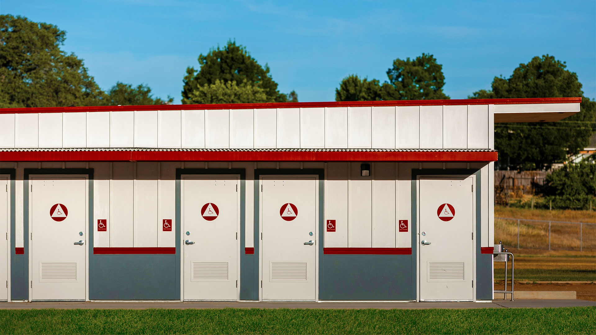 Portable restroom building with white panel walls and gray wainscot, with concrete walkway and grass.