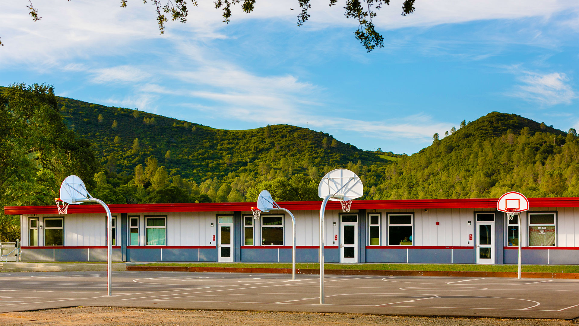 Renovated portables against green hill background. Basketball court in foreground.