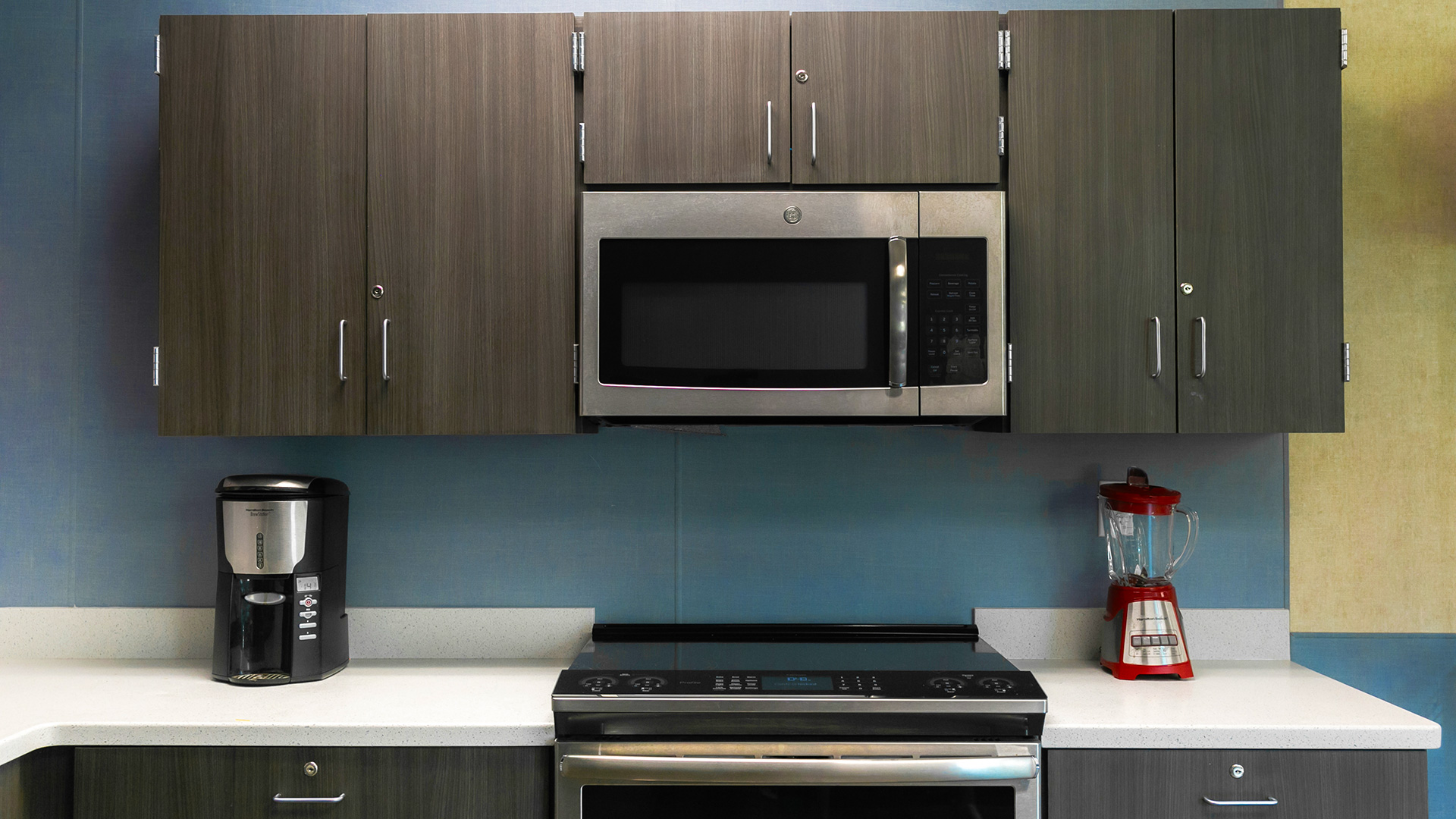 Kitchen area in a portable classroom, with blue walls and gray cabinets.