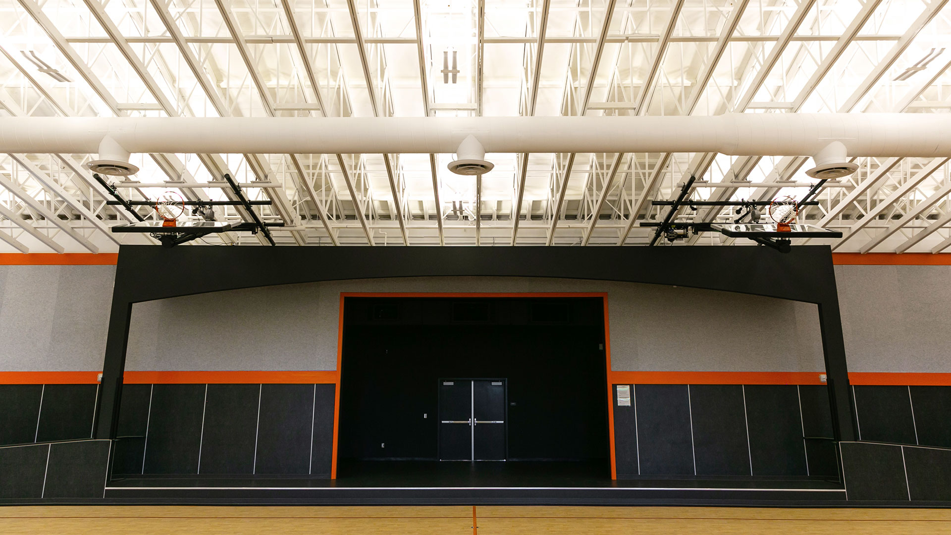 Interior of gym, highlighting lifted stage integrated between classrooms and adjacent to the basketball court.