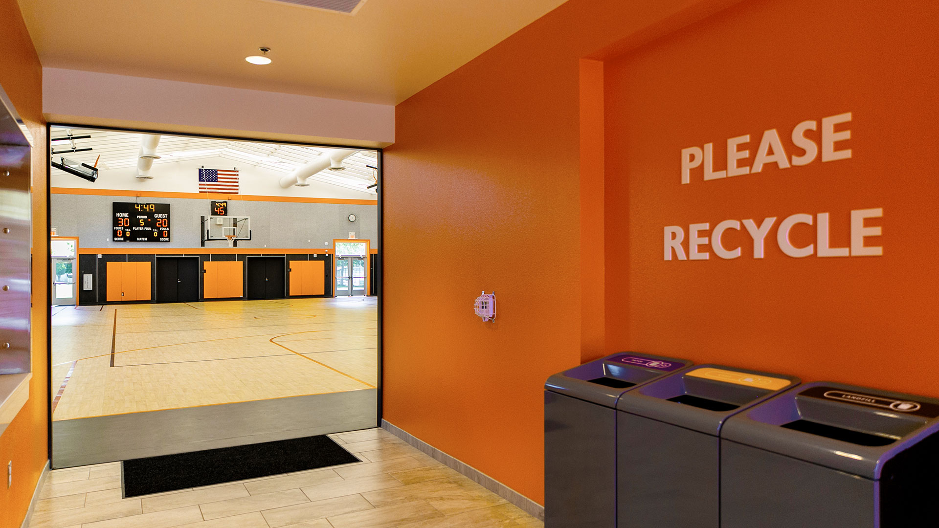 Interior of hallway between foyer and gym, with orange walls and a recycle and trash hub.