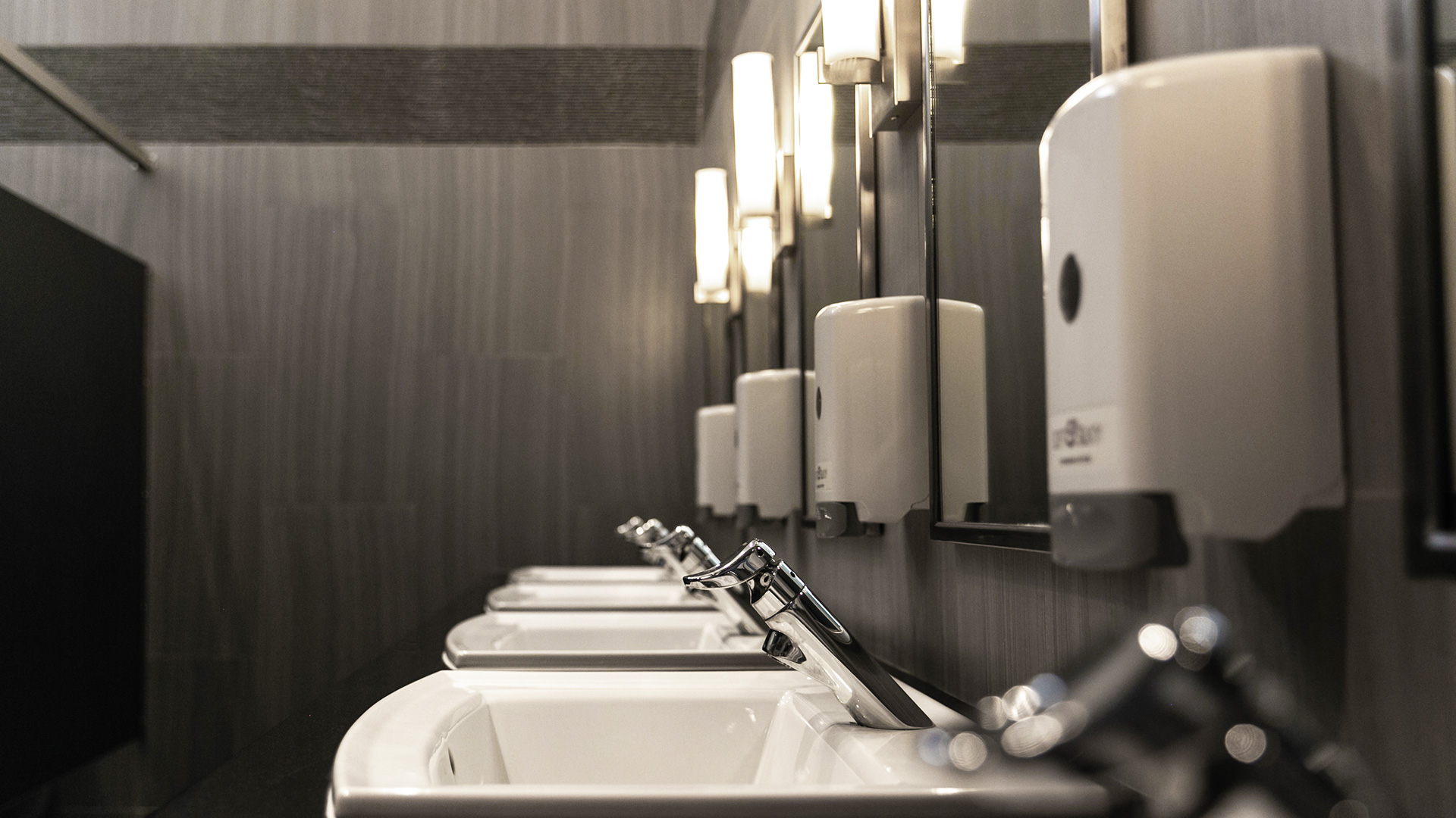 Bathroom, with textured panel gray walls and black trim, sleek wall light in between mirrors above sinks.