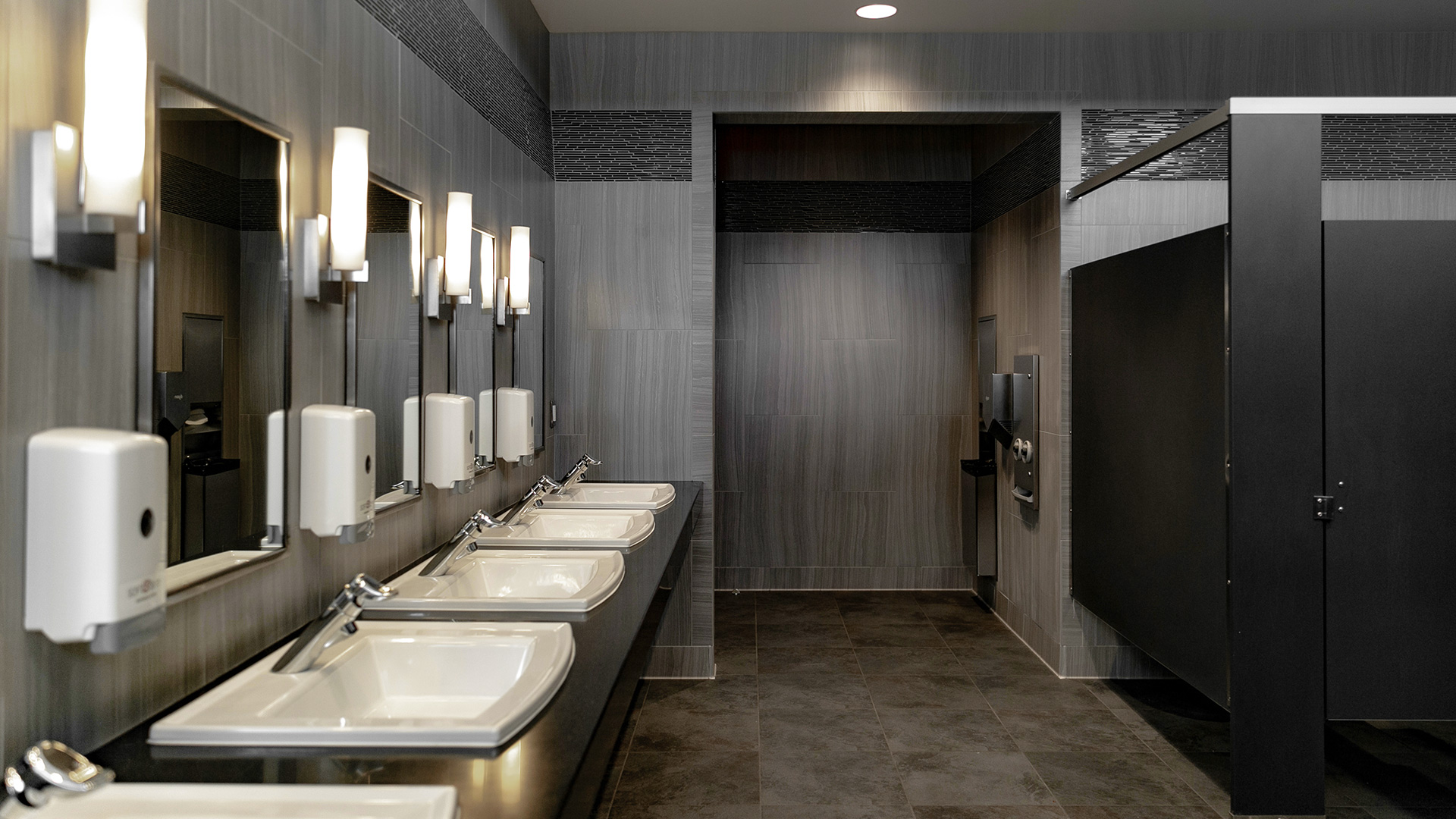 Bathroom, with textured panel gray walls and black trim, looking at entrance with hand dryers.