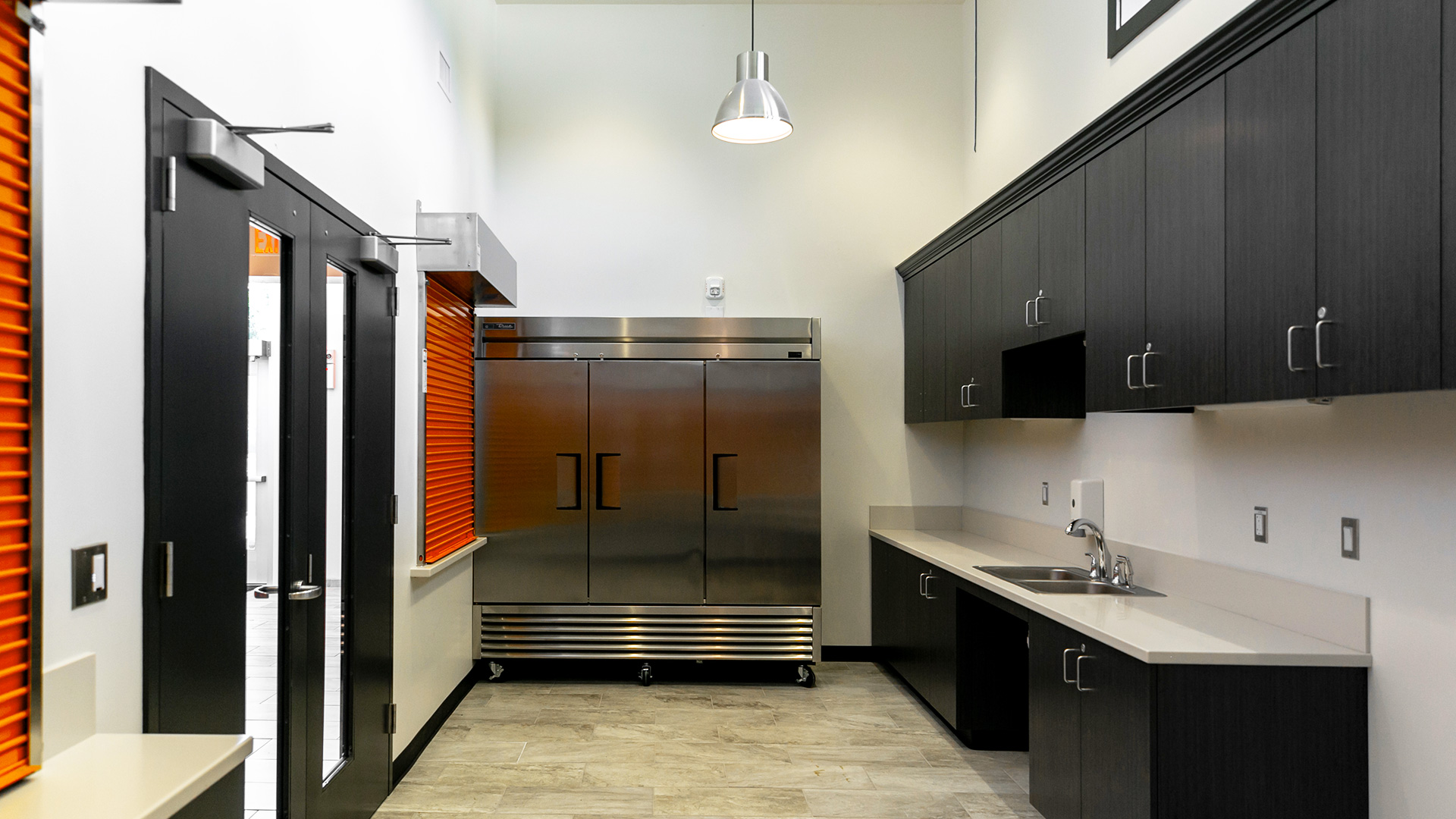 Full kitchen located in the snack shack. Double height white ceilings and walls with black cabinetry.