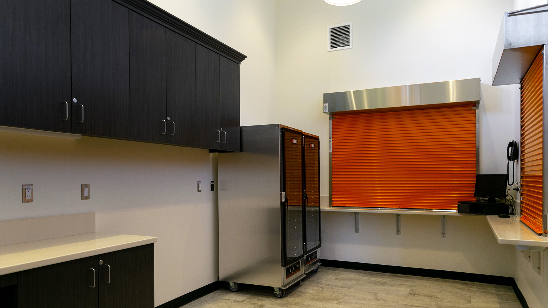 Full kitchen located in the snack shack. White walls and black cabinetry juxtaposed with bright orange roll-up doors.