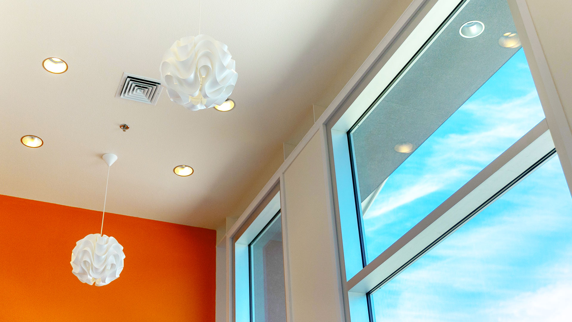 Interior of foyer, looking up at windows reaching the ceiling and textured sphere light fixtures hanging above.