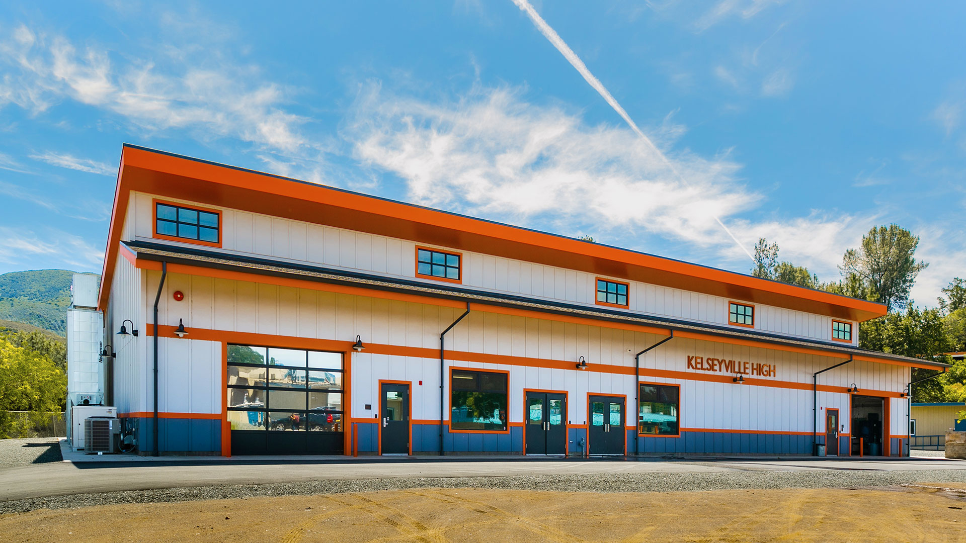 Exterior of shop building, white wood with orange trim and gray wainscot. Blue sky above.