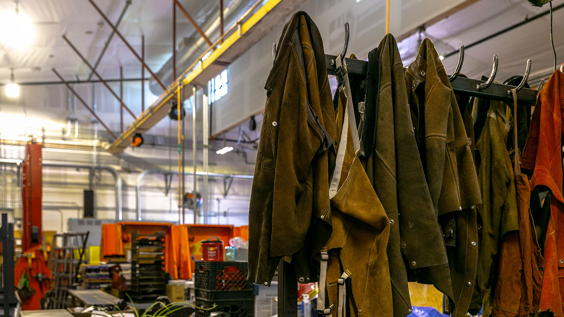 Shop interior with heavy brown welding jackets in foreground of welding booths.