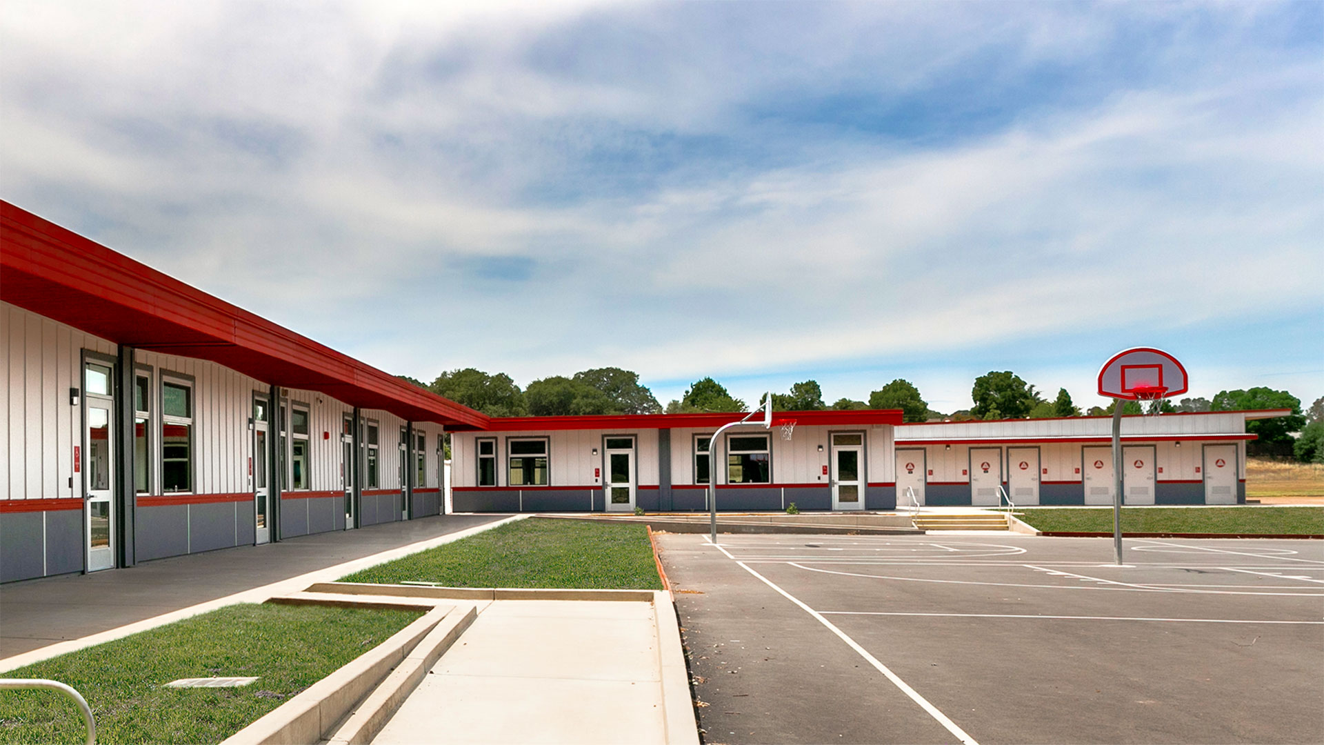 Portable classroom wing with white panel walls and gray wainscot, with concrete walkways and grass.