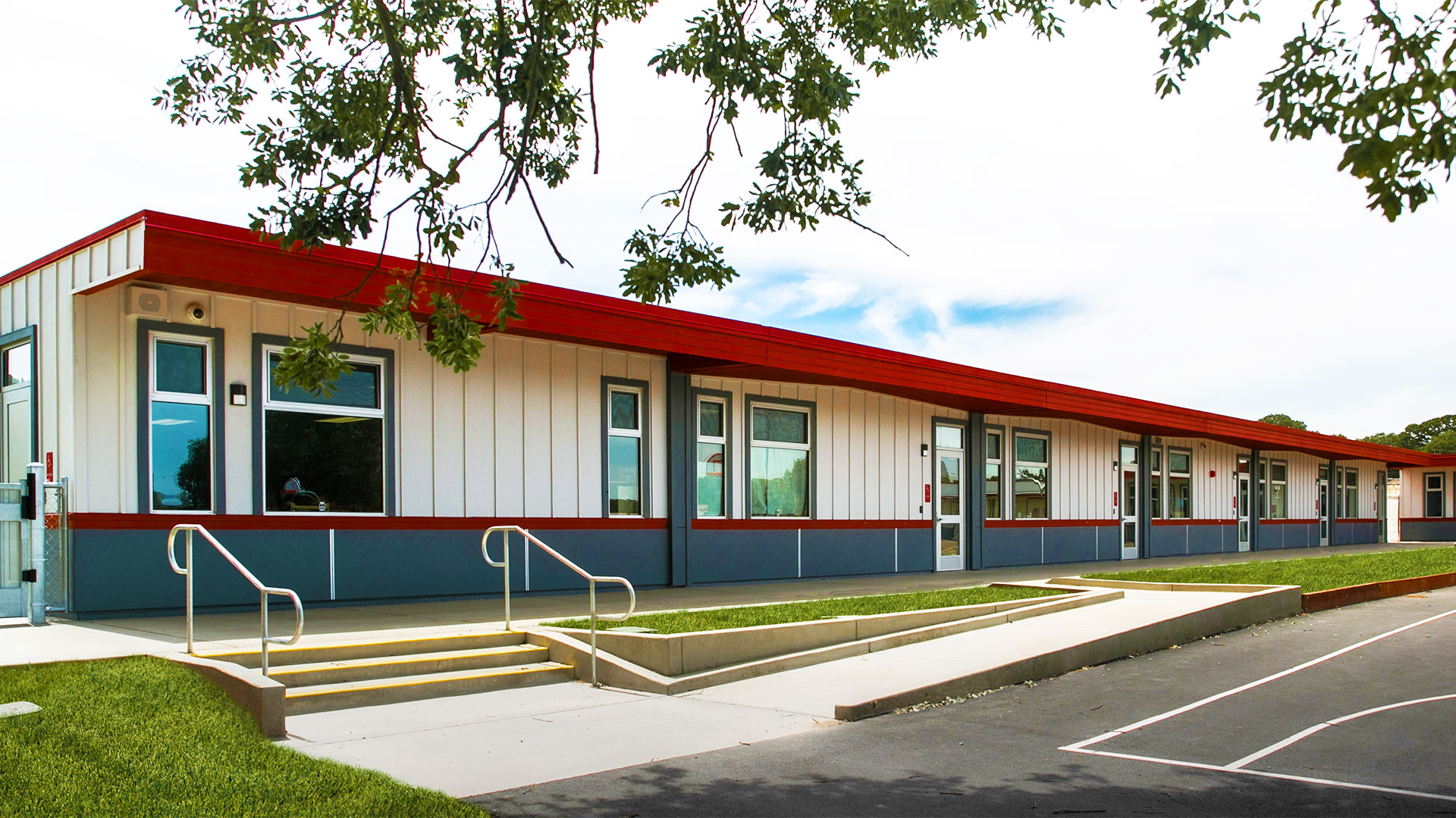 Portable classroom wing with white panel walls and gray wainscot, with concrete walkway and grass.