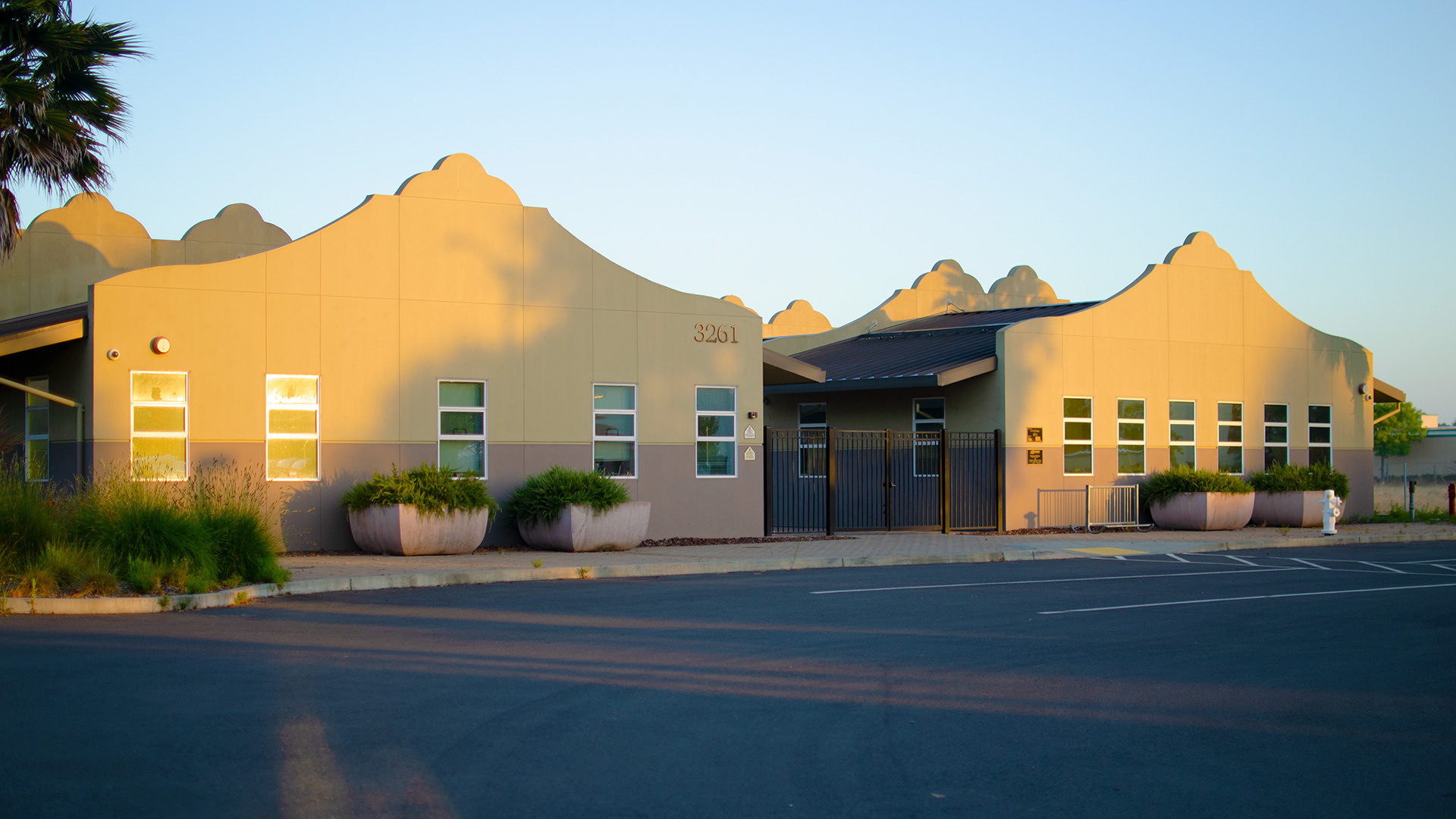 Entrance of school, with mission-style rooflines, beige walls, and gray wainscot. Front entrance is gated.
