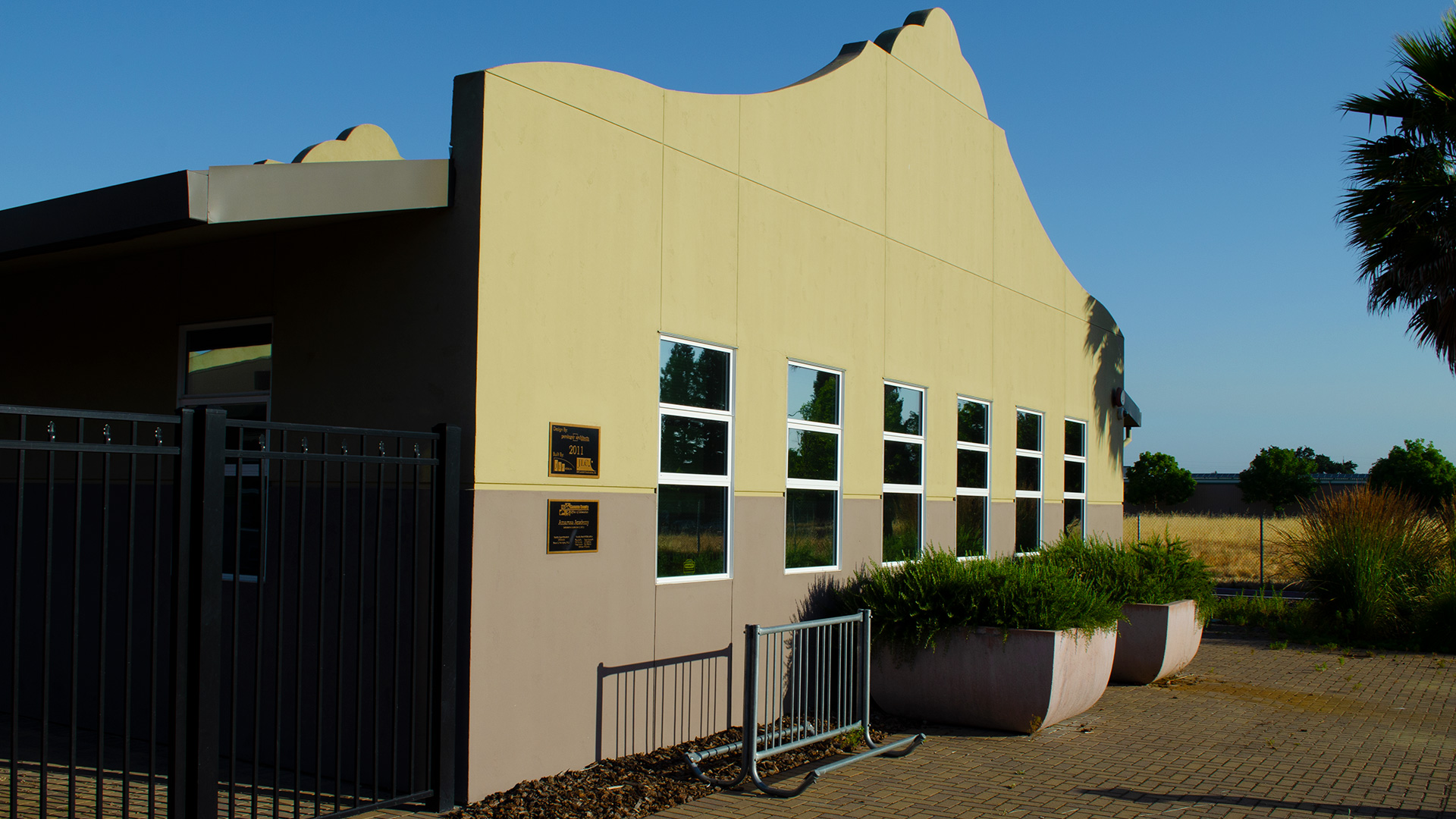 Entrance of school, with mission-style rooflines, beige walls, gray wainscot, and a bike rack in front..