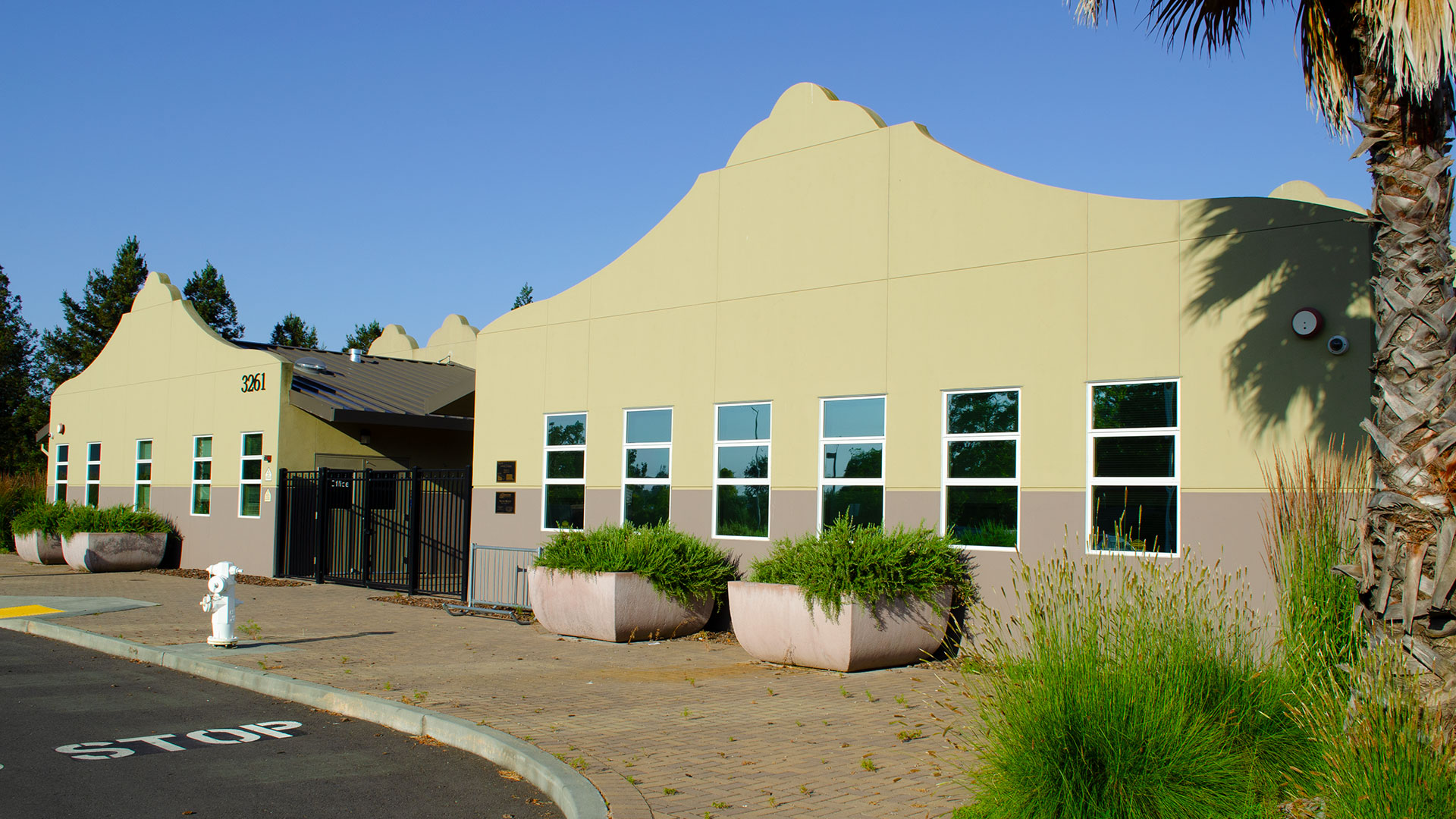Entrance of school, with mission-style rooflines, beige walls, and gray wainscot. Front entrance is gated.