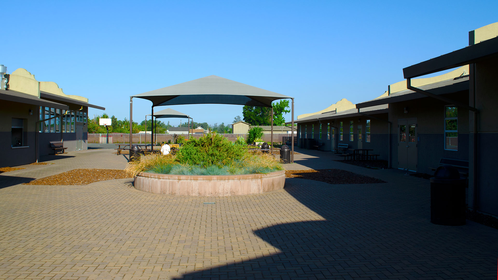 School courtyard with brick planter and seats. Shade structure in back over seating area.