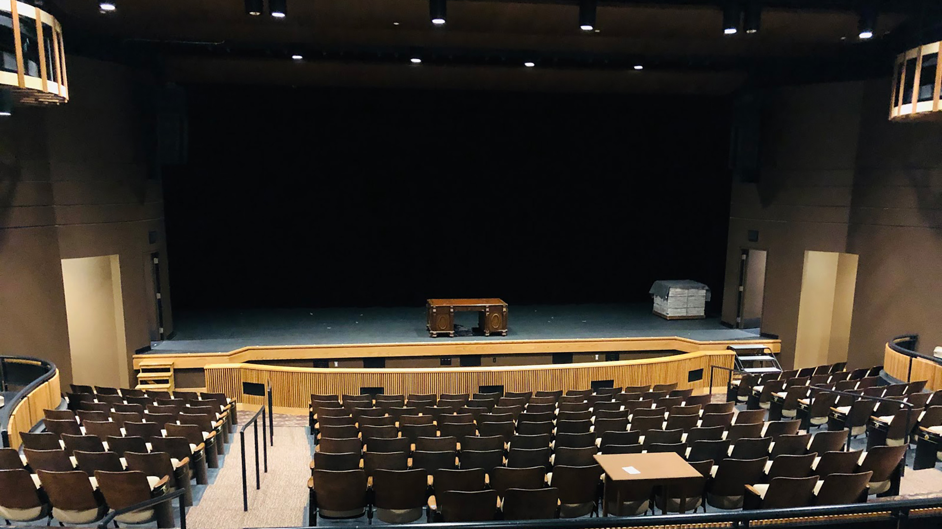 Stage in performing arts center, sections of seats look towards elevated platform with black curtains