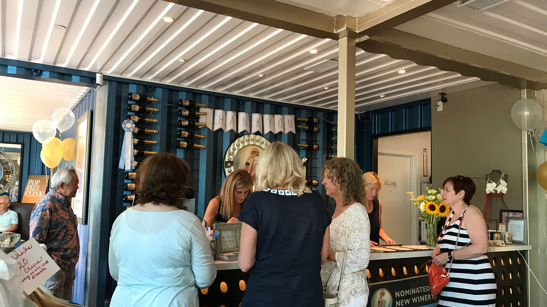 Serving counter in completed tasting room with patrons, currogated blue walls and white ceilings.