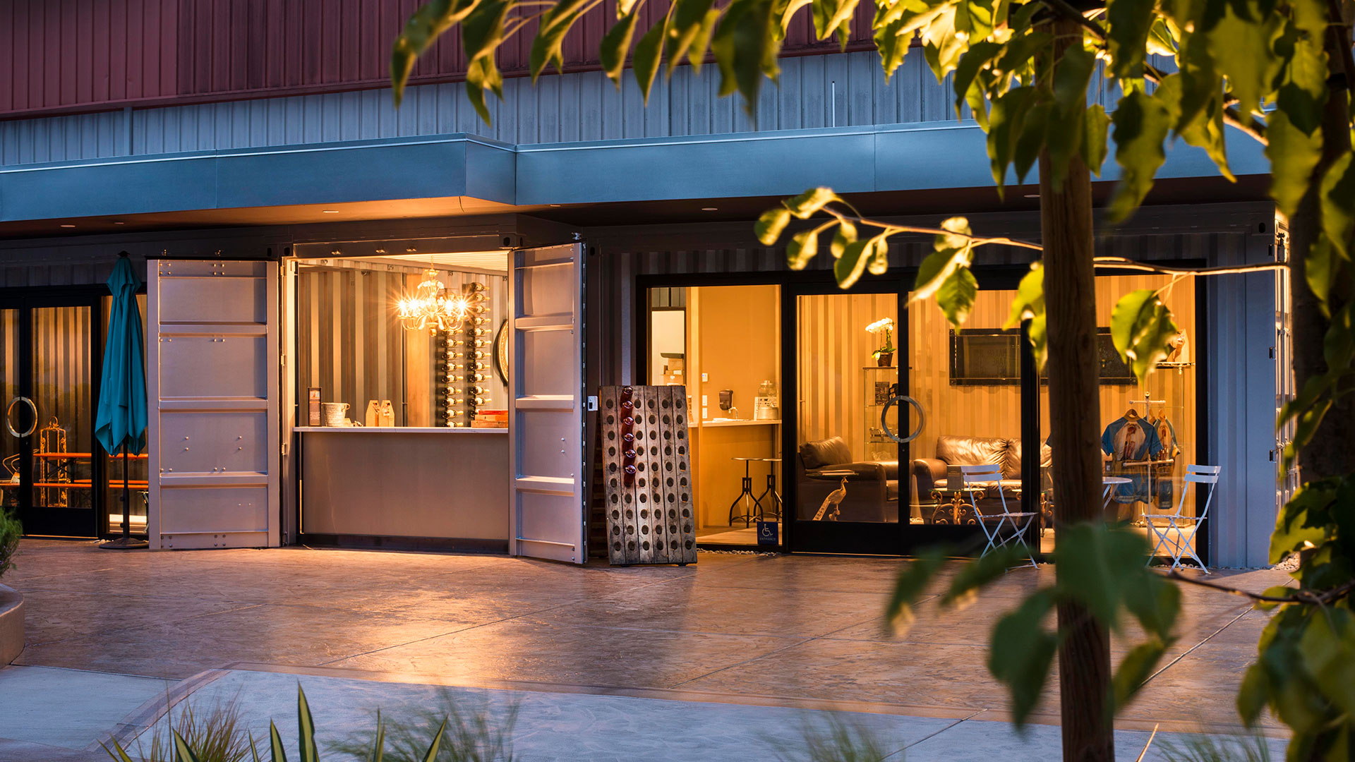Exterior of tasting room at night, light illuminating through windows and shipping container doors open to serving area.