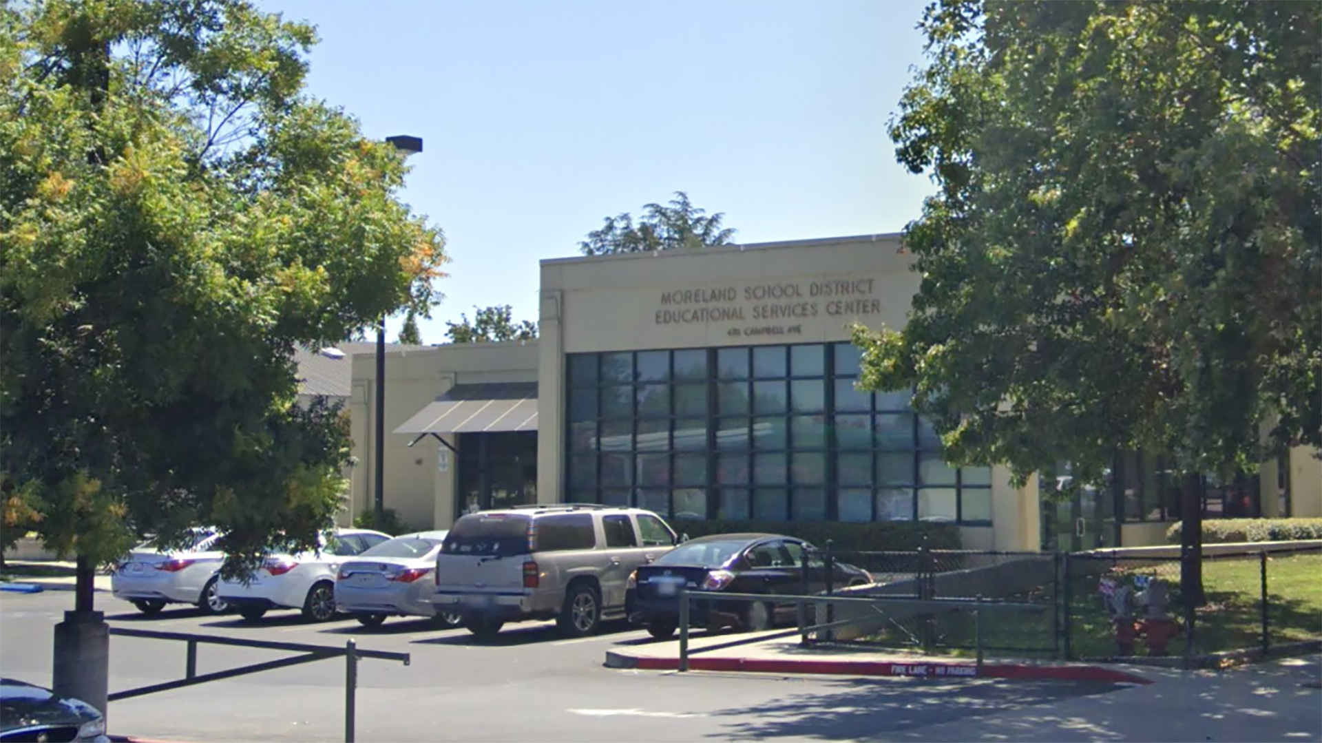 Exterior of office building, with large wall of windows and parking lot in front.