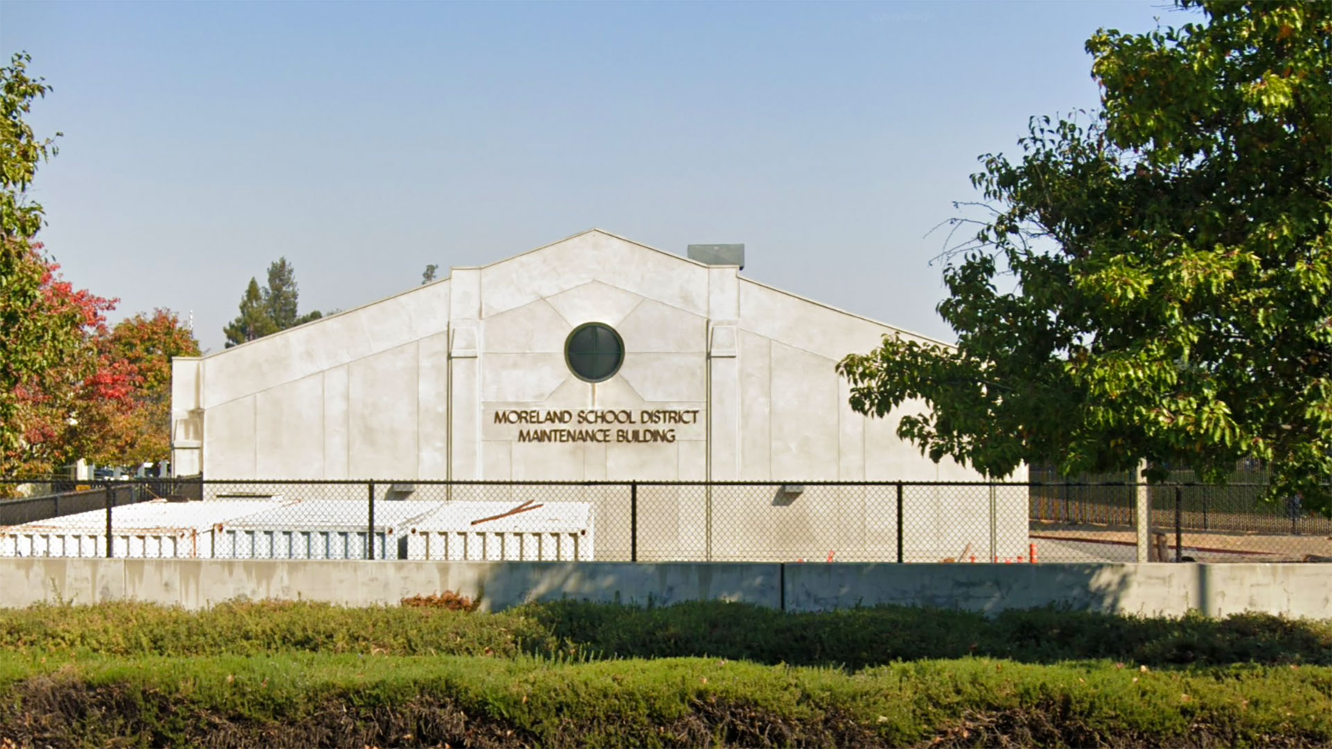 Exterior of concrete maintenance building with gable roof and circular window centered at wall peak.