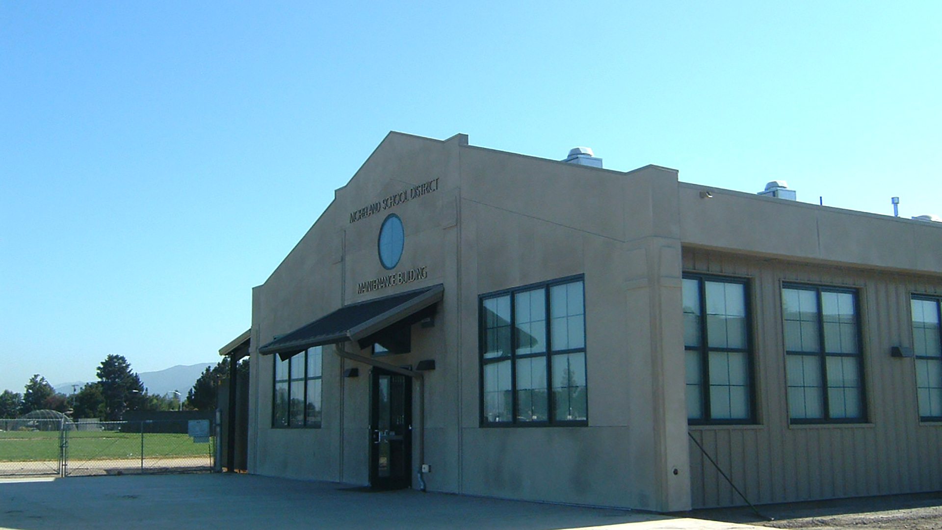 Exterior of concrete maintenance building with gable roof and circular window centered at wall peak.