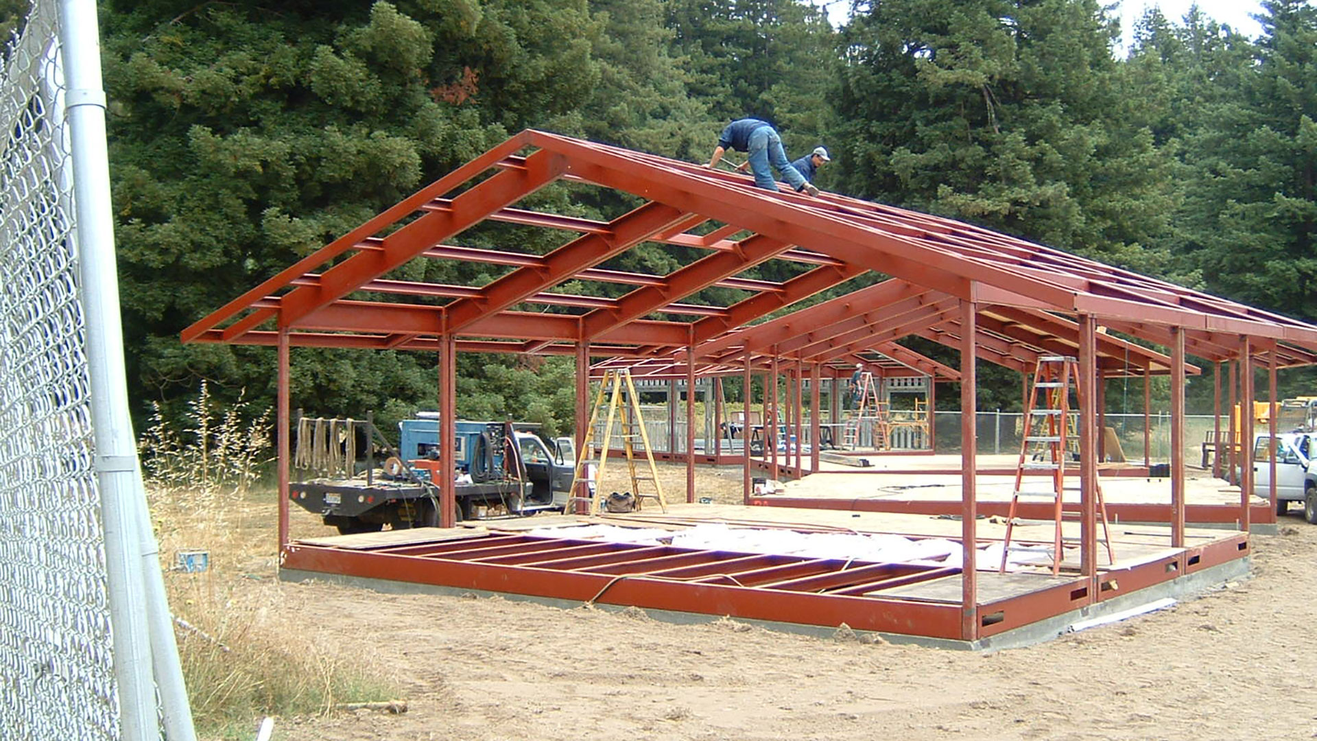 Exposed red metal frame during construction of several buildings side-by-side.