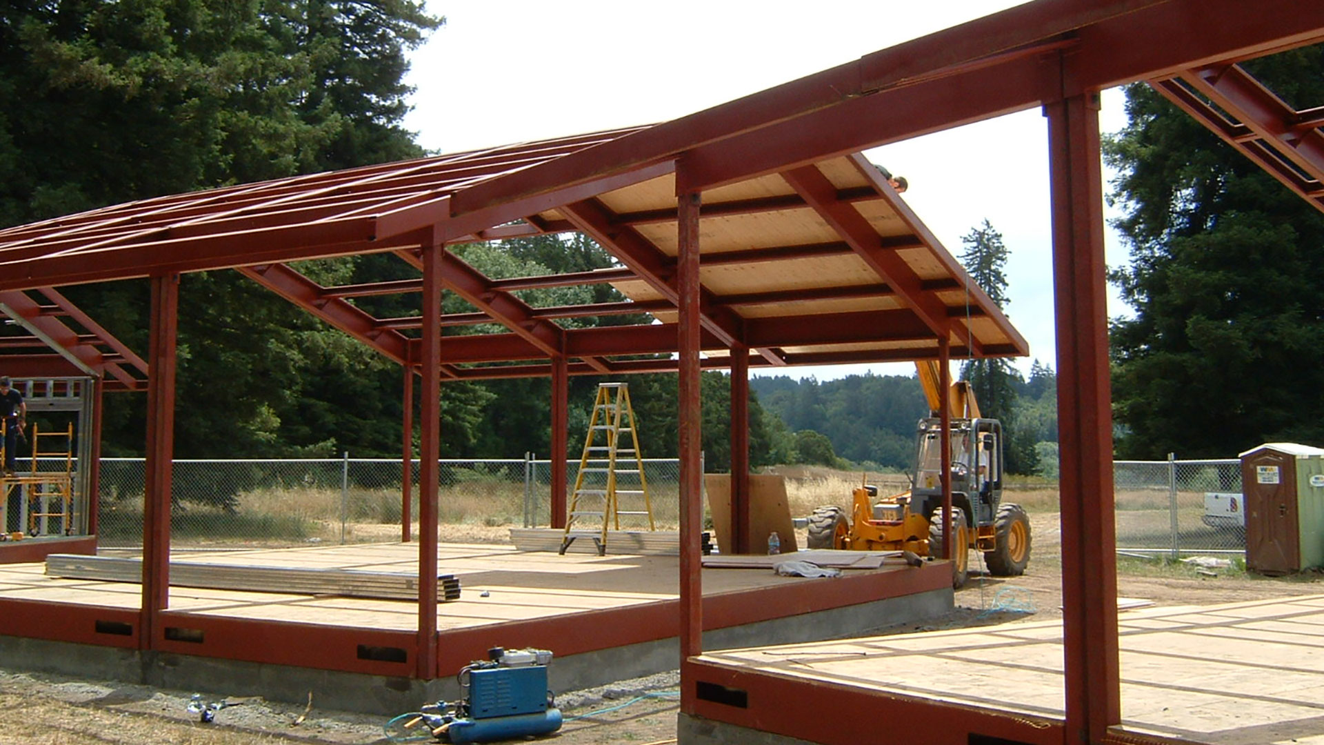 During construction, exposed red metal frame with plywood roof being installed.