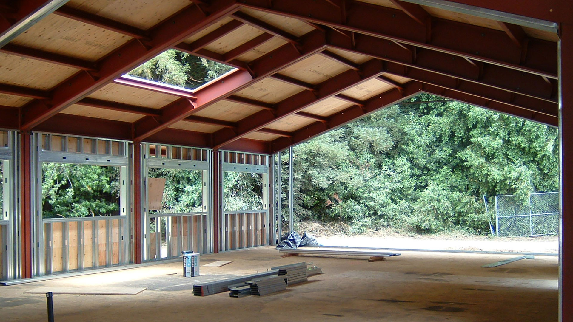 Roof installed on the red metal frame, with holes for skylight, and walls being installed.