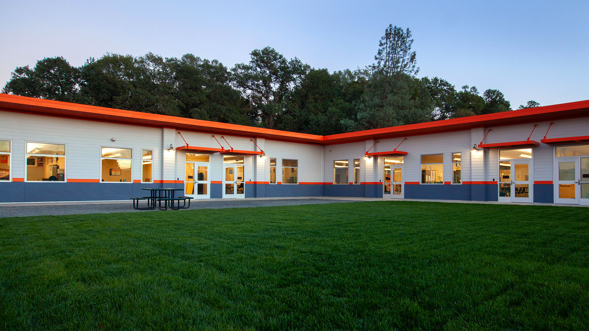 Classroom wing with white walls, gray wainscot, and orange trim in front of grass field.
