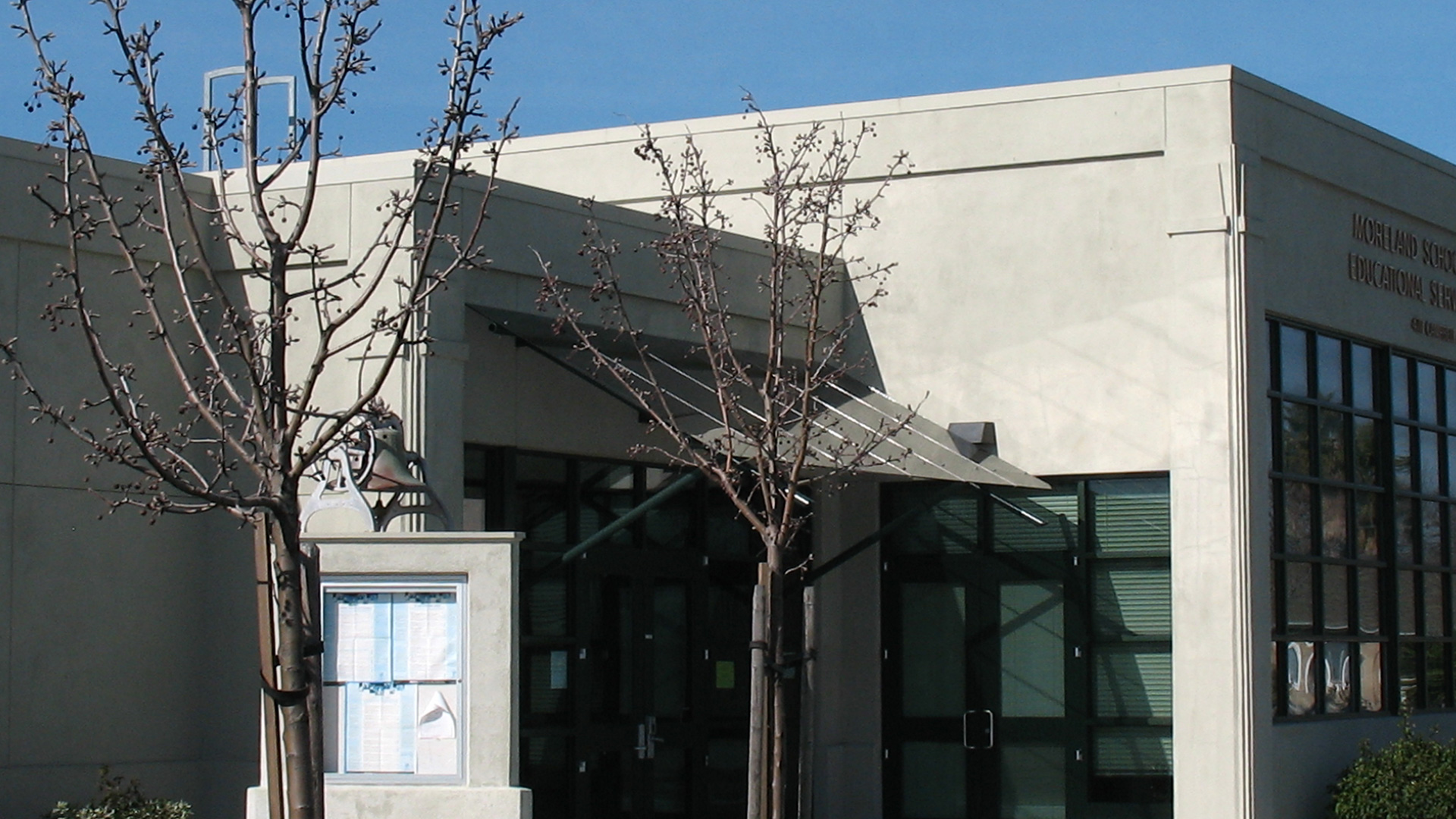 Entrance to district office, with glass awning, trees, and directory in front.