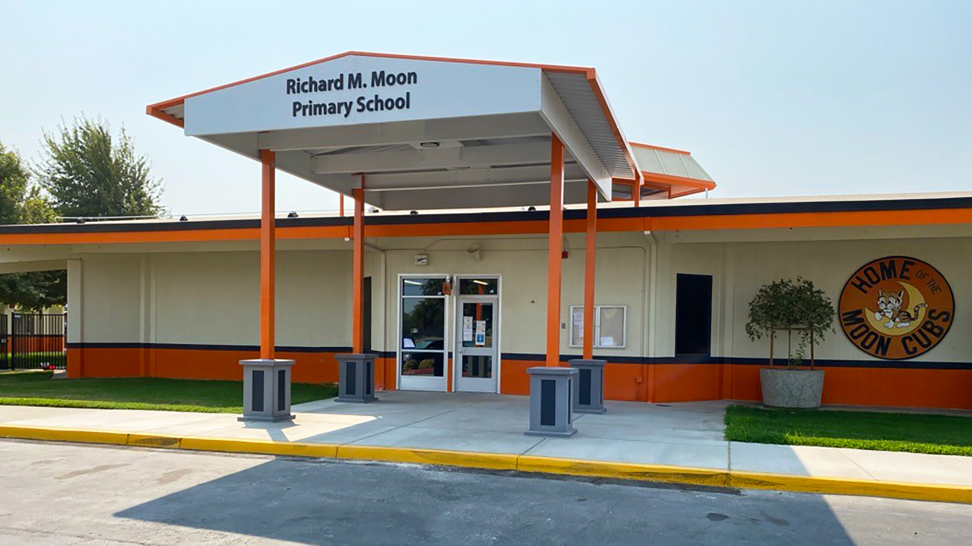 New orange and white painted building behind orange and white entry shade structure with the school name in lettering,