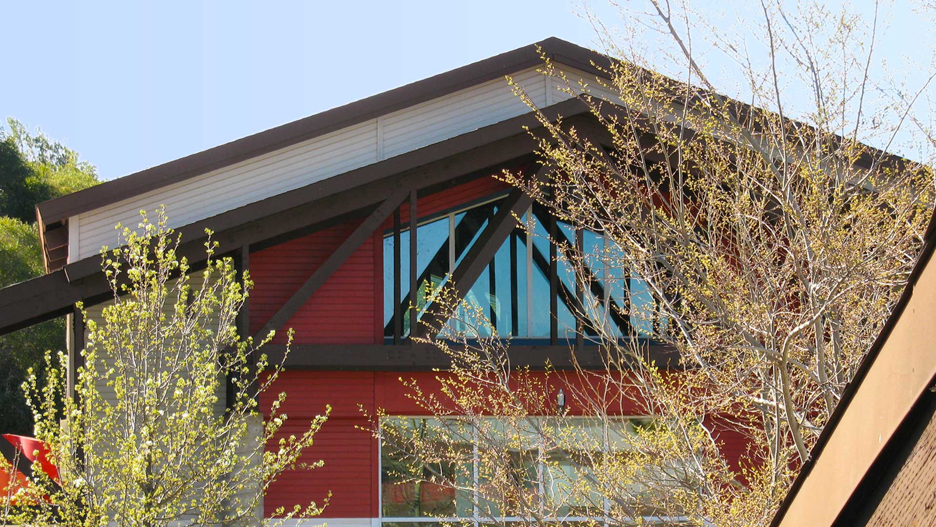 Roofline of building with exposed trusses in front of red walls and large windows.