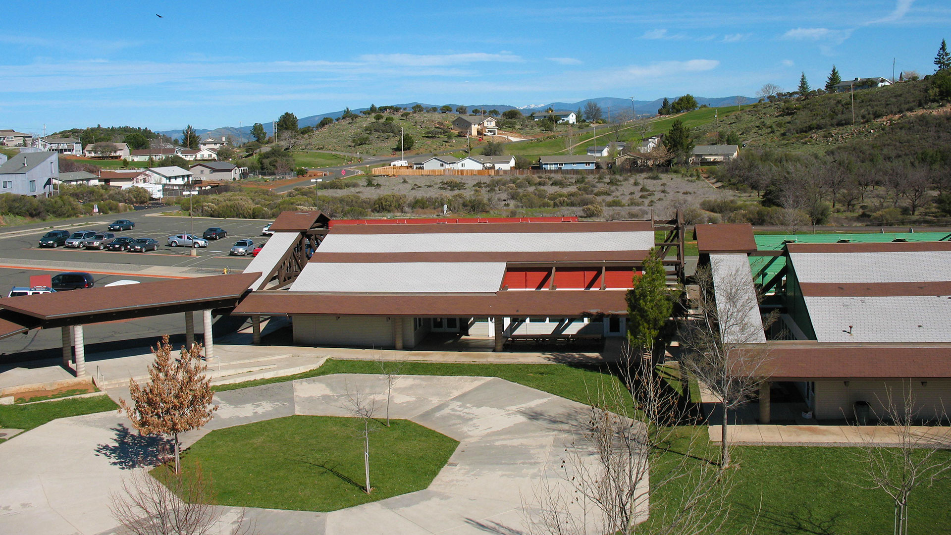 Campus courtyard with circular concrete walkway, and building with expansive white and brown roof behind.