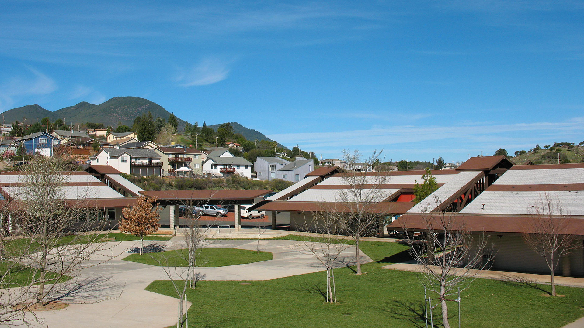 Campus courtyard with circular concrete walkway, and building with expansive white and brown roof behind.